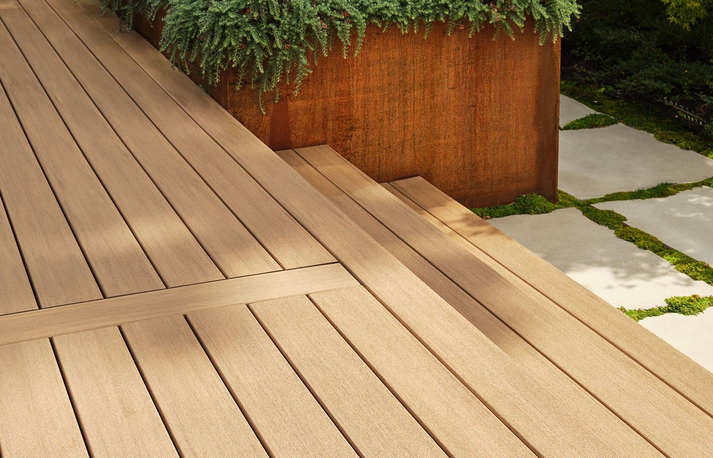 Wooden deck with steps, next to a rusty planter with greenery, and stone pathway.