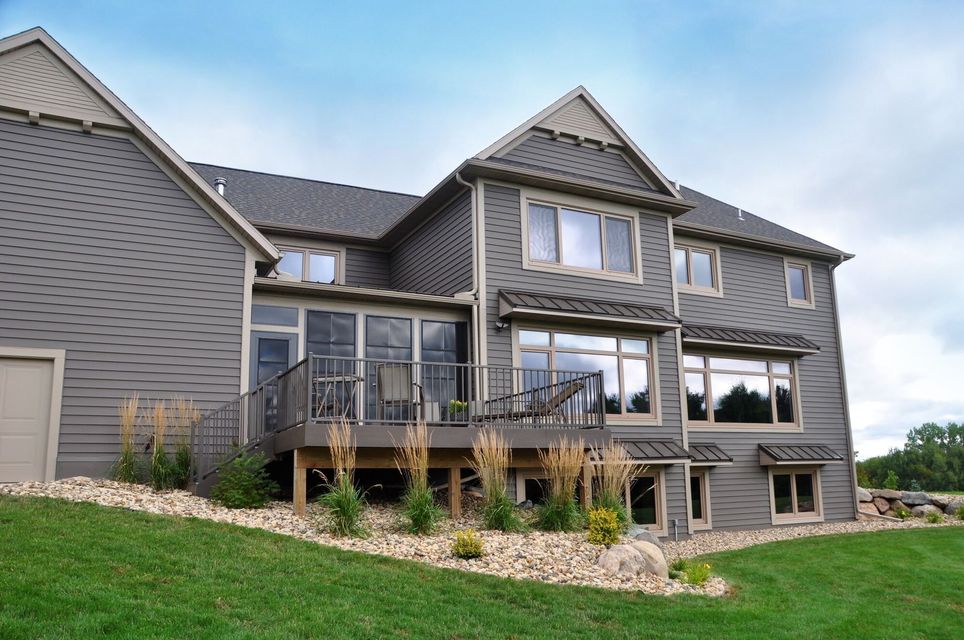 Two-story gray house with a deck and windows, landscaping, and a green lawn.