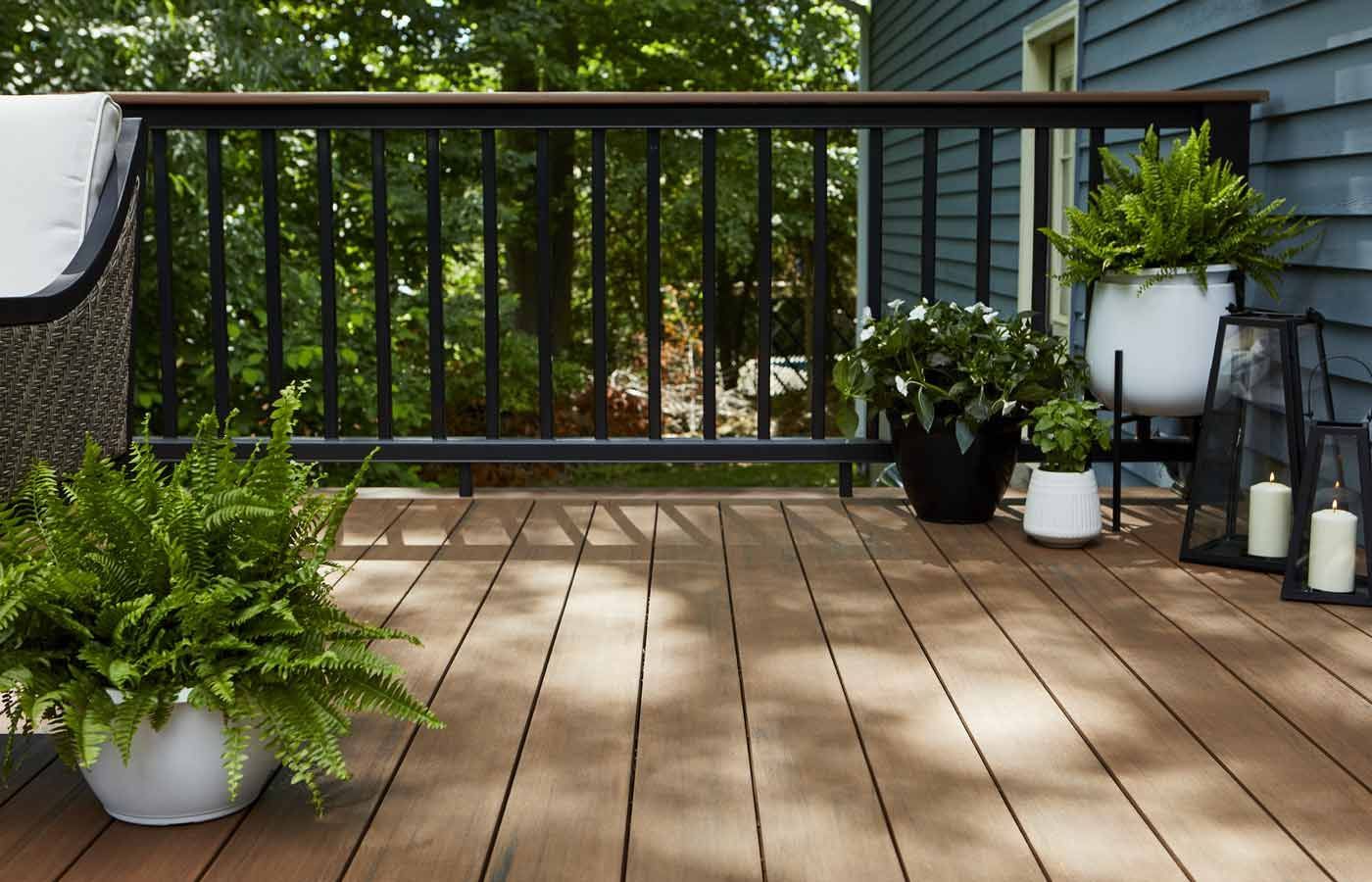 Wooden deck with black railing, potted plants, and a view of trees.