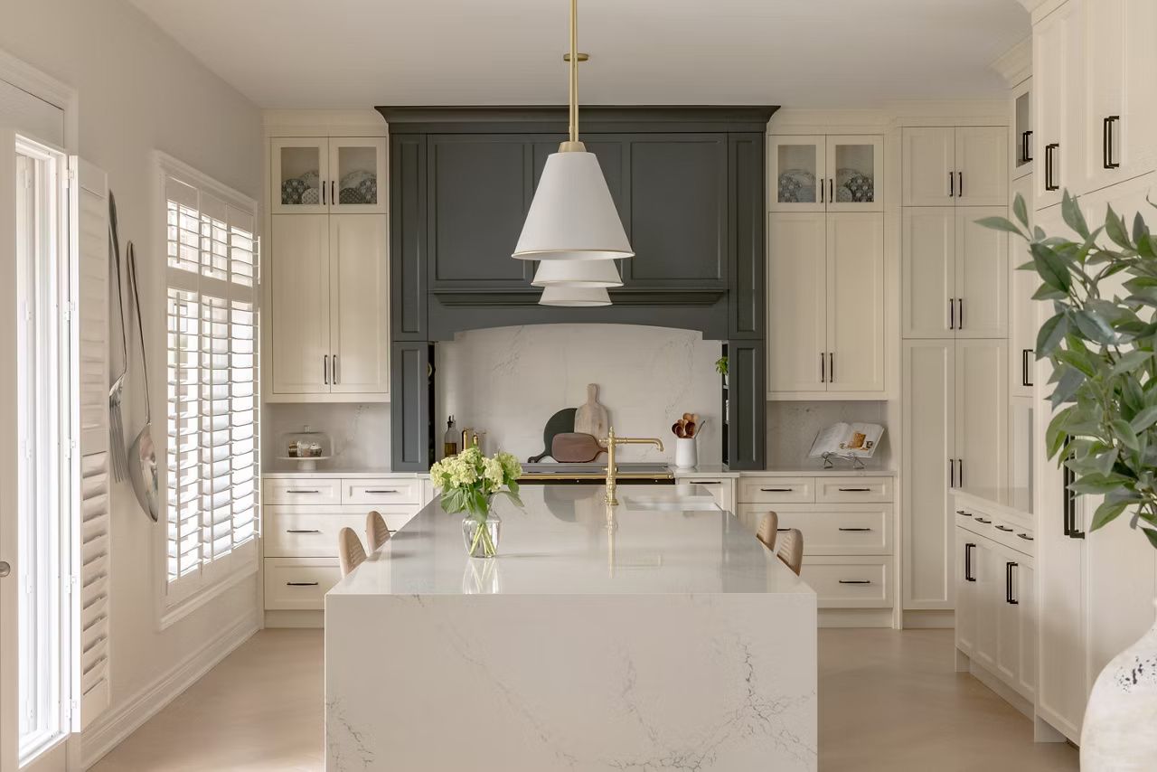 Elegant white kitchen with a dark gray range hood, central island, and pendant light.