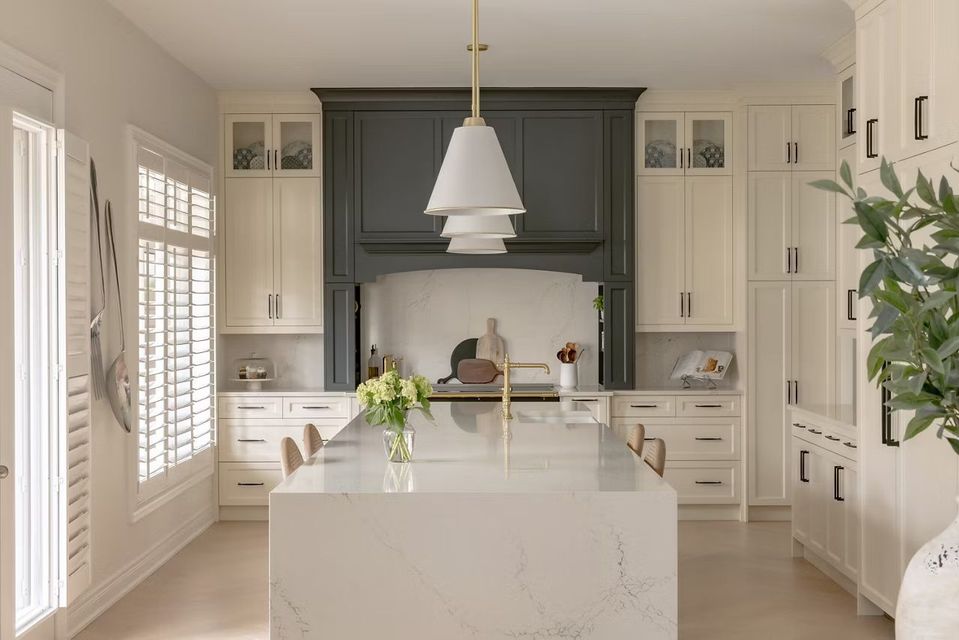 Elegant white kitchen with a gray range hood, large island, and pendant light.