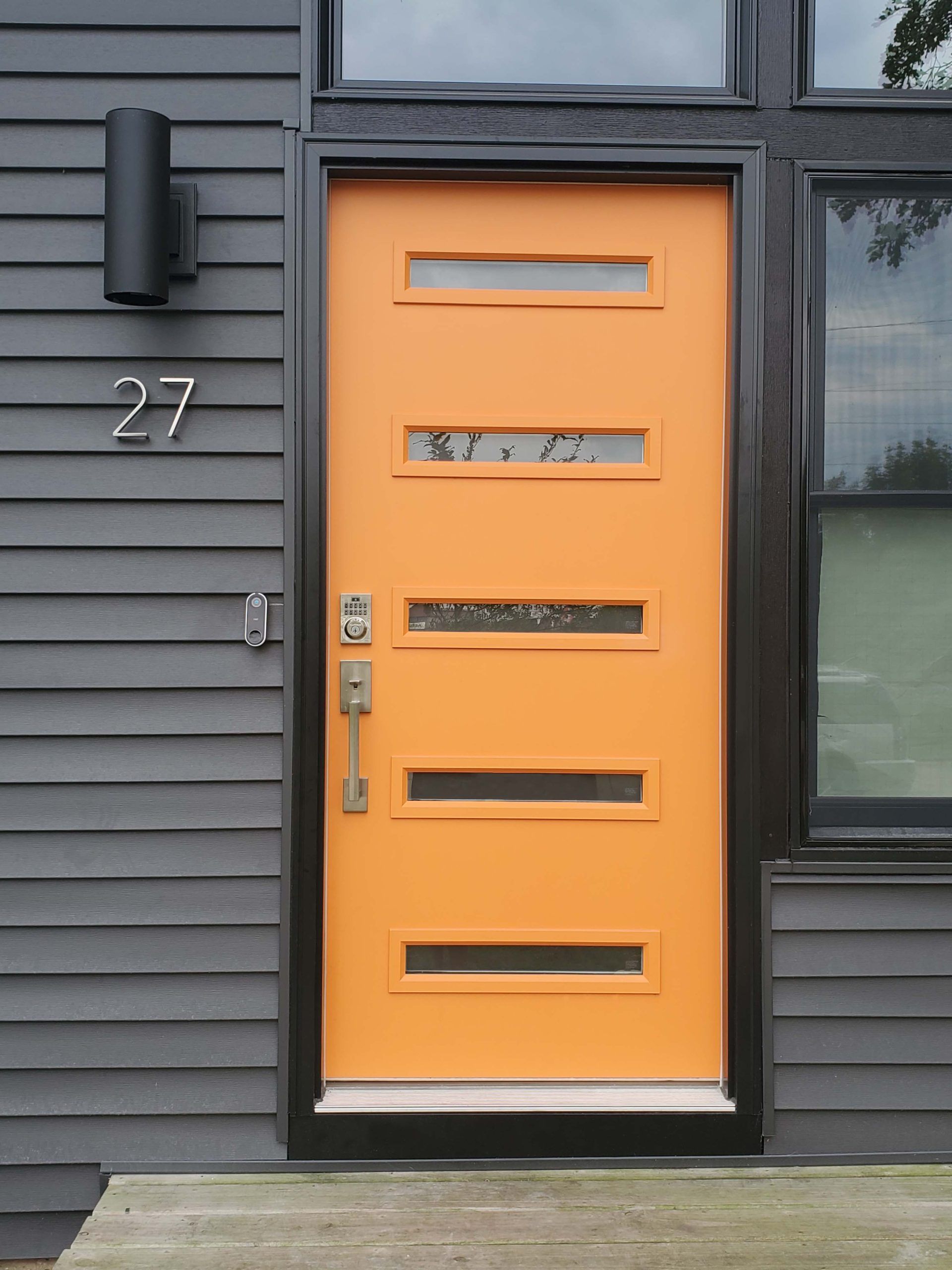 Orange front door with horizontal windows and black trim. House number