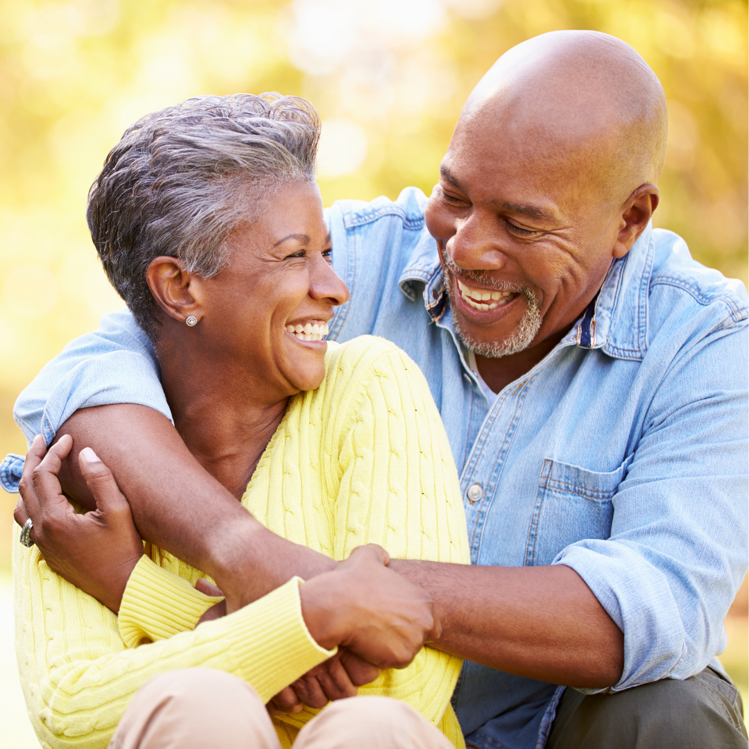 A man and woman are hugging each other and smiling . the woman is wearing a yellow sweater.
