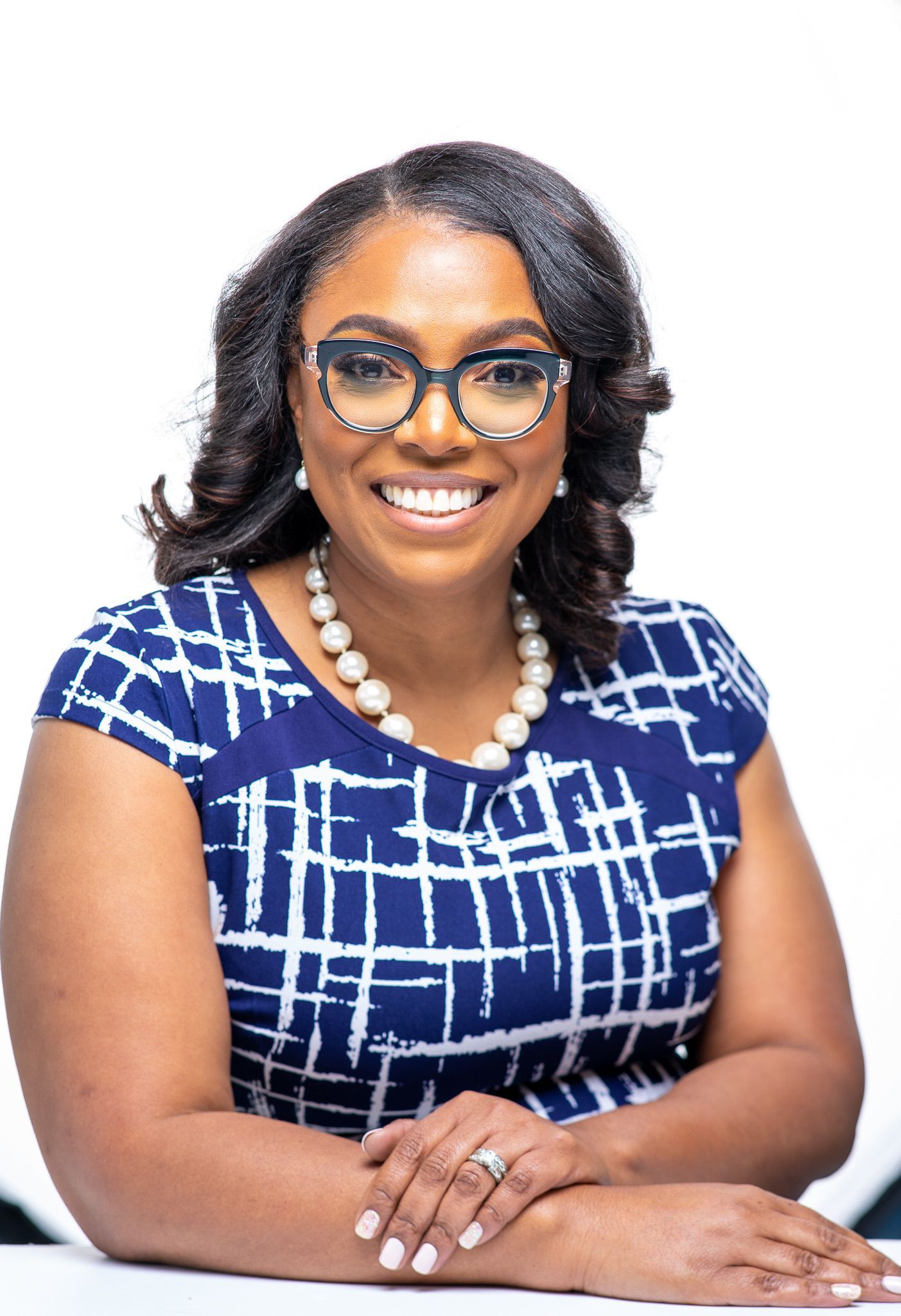 Smiling woman with glasses wearing a blue and white patterned top and pearl necklace.