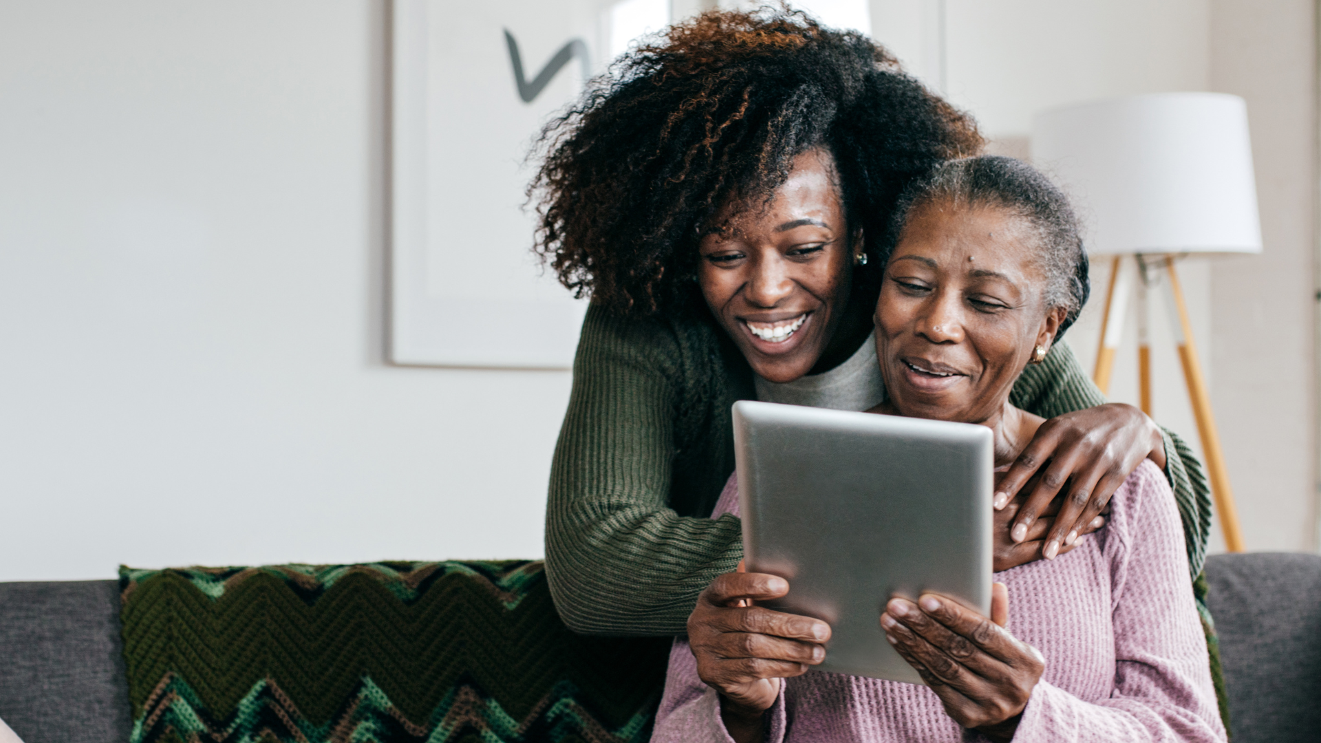 Two women are sitting on a couch looking at a tablet.