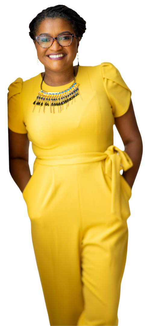 A woman in a yellow jumpsuit and glasses is standing with her hands in her pockets.