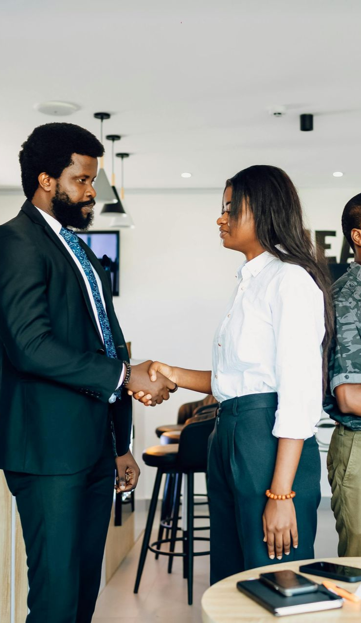 Man in suit shakes hands with woman in white shirt in an office.