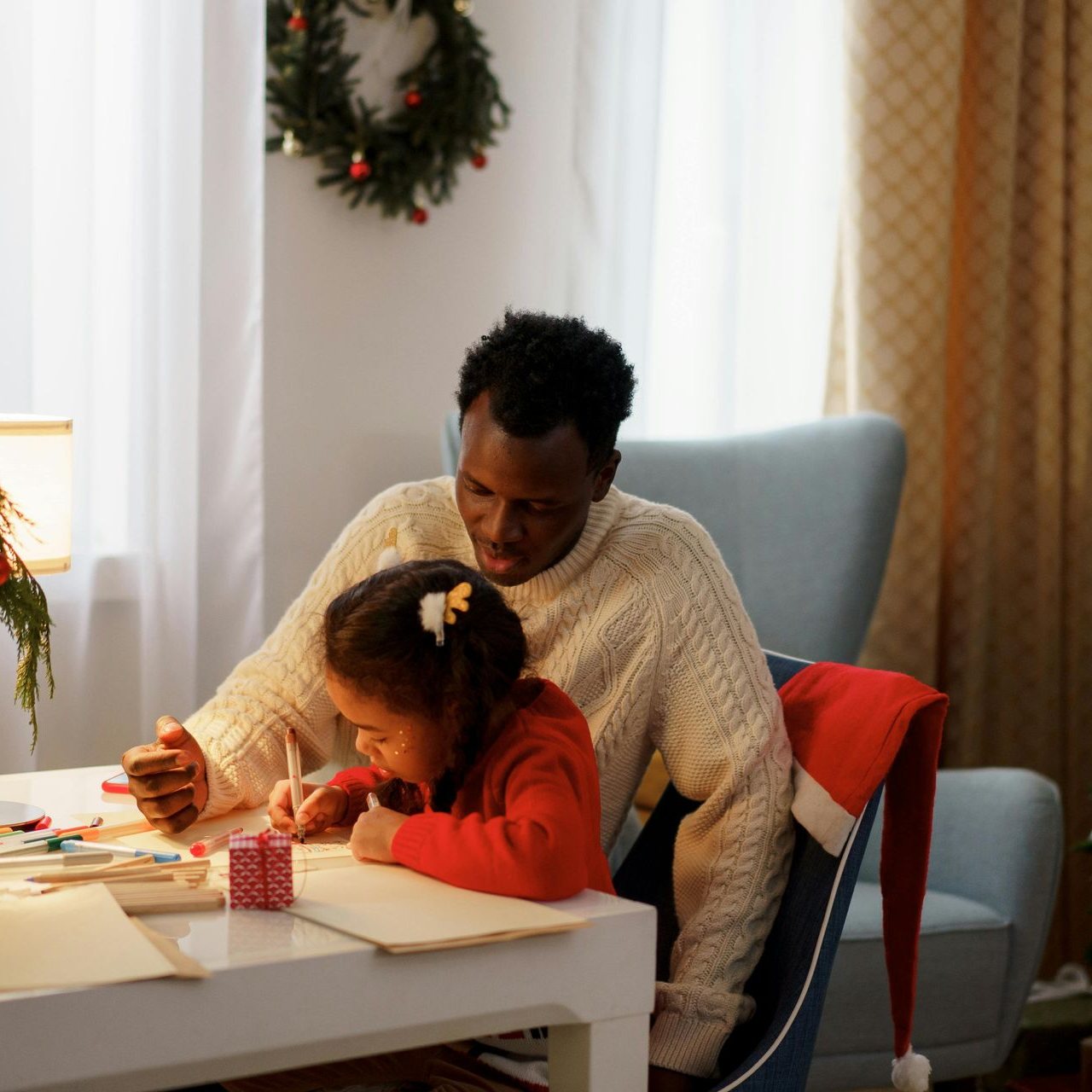 Man and child sitting at a table, writing. Christmas decorations visible in background.