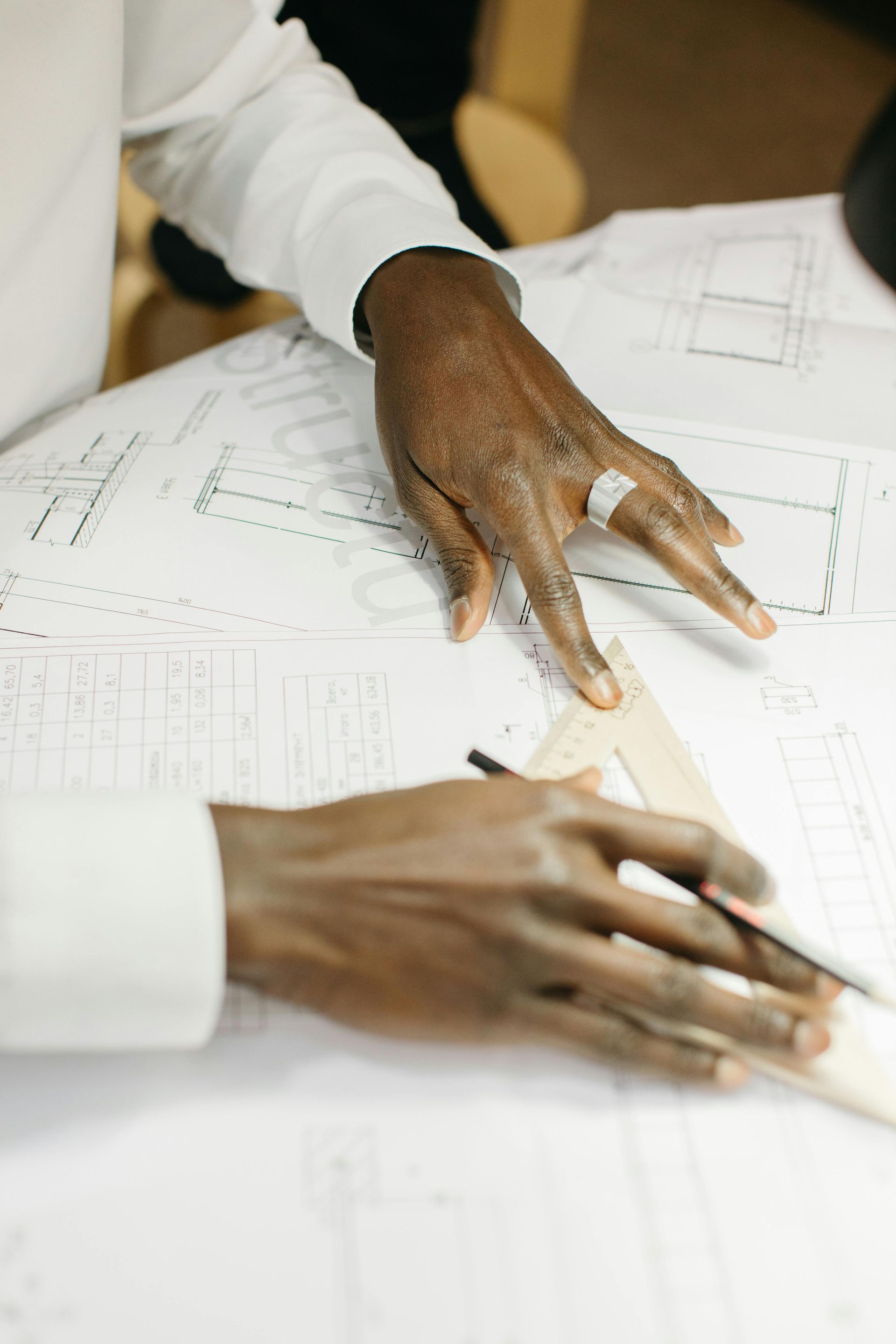 Hands of a person using a ruler and pencil on architectural plans, likely for a building project.