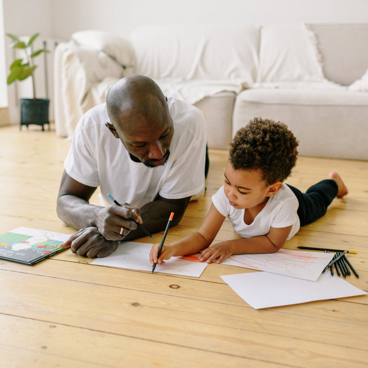 A man and a child are laying on the floor drawing with pencils.