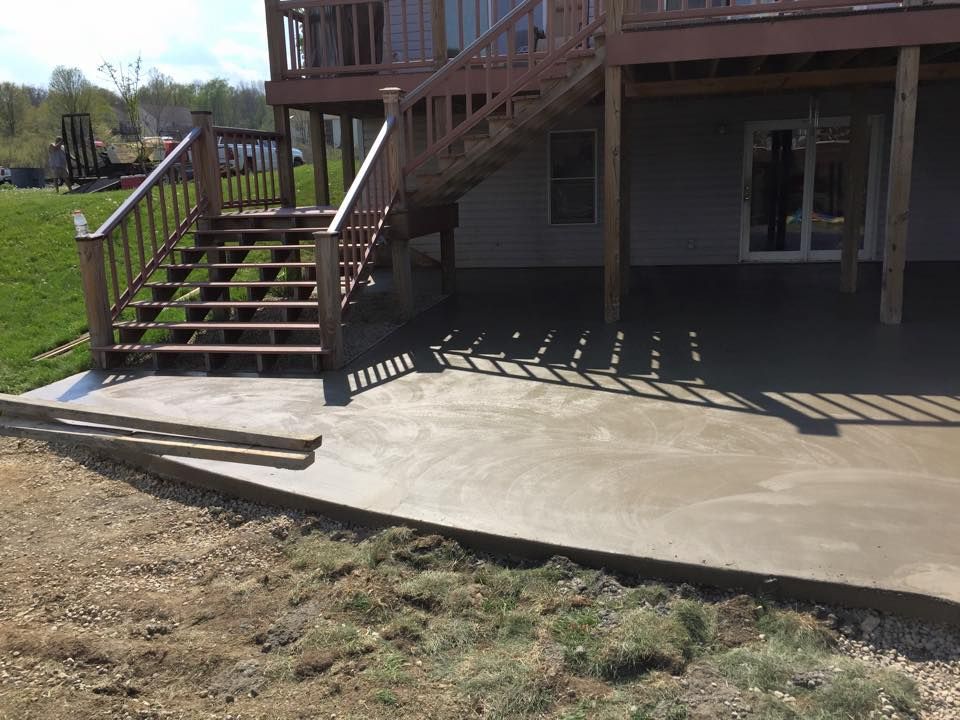 A concrete patio in front of a house with stairs and a deck.