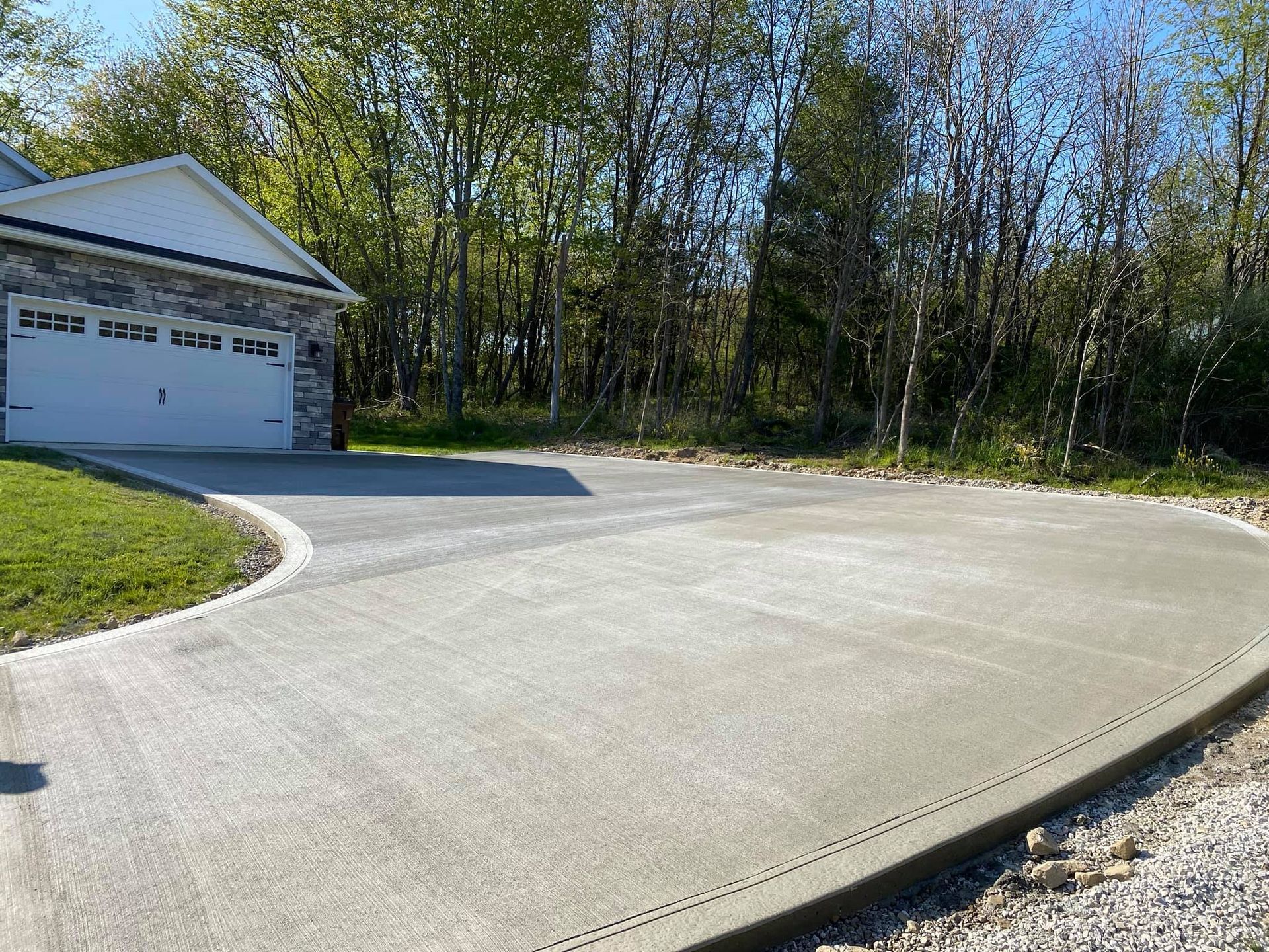A concrete driveway leading to a house with trees in the background.