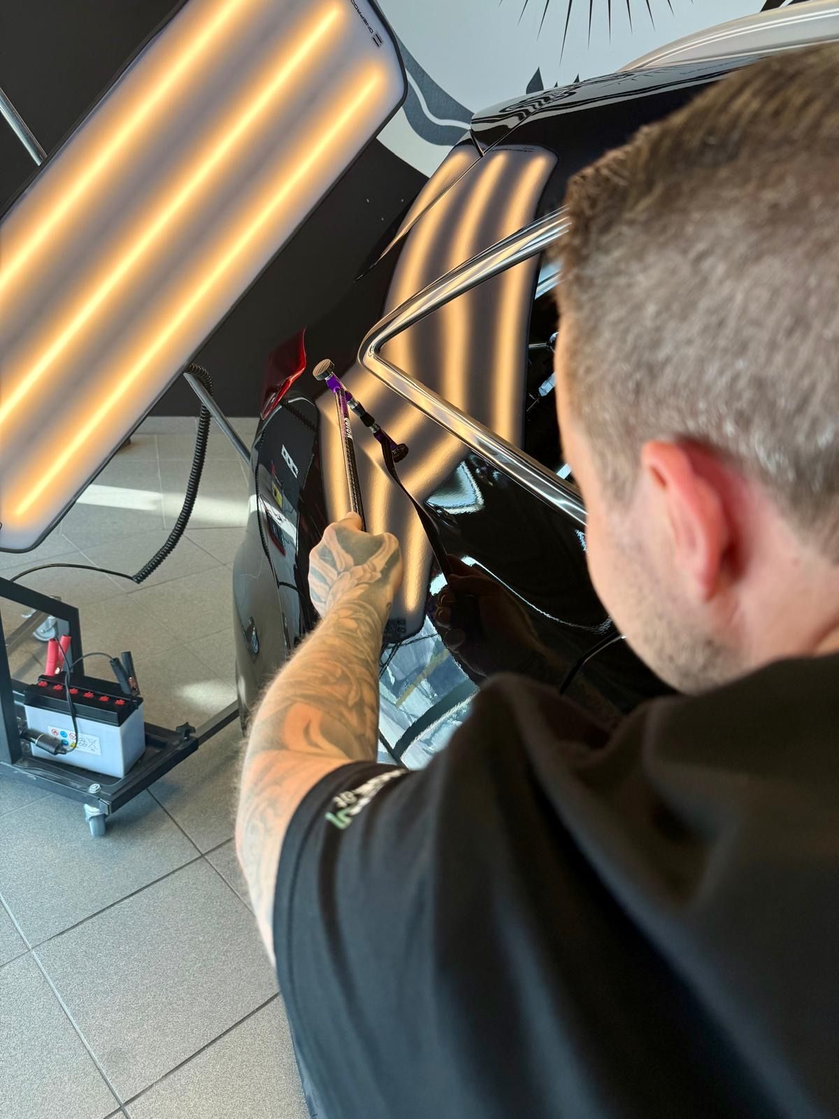 Ein Mann arbeitet an einem Auto, hinter ihm ist ein Licht.