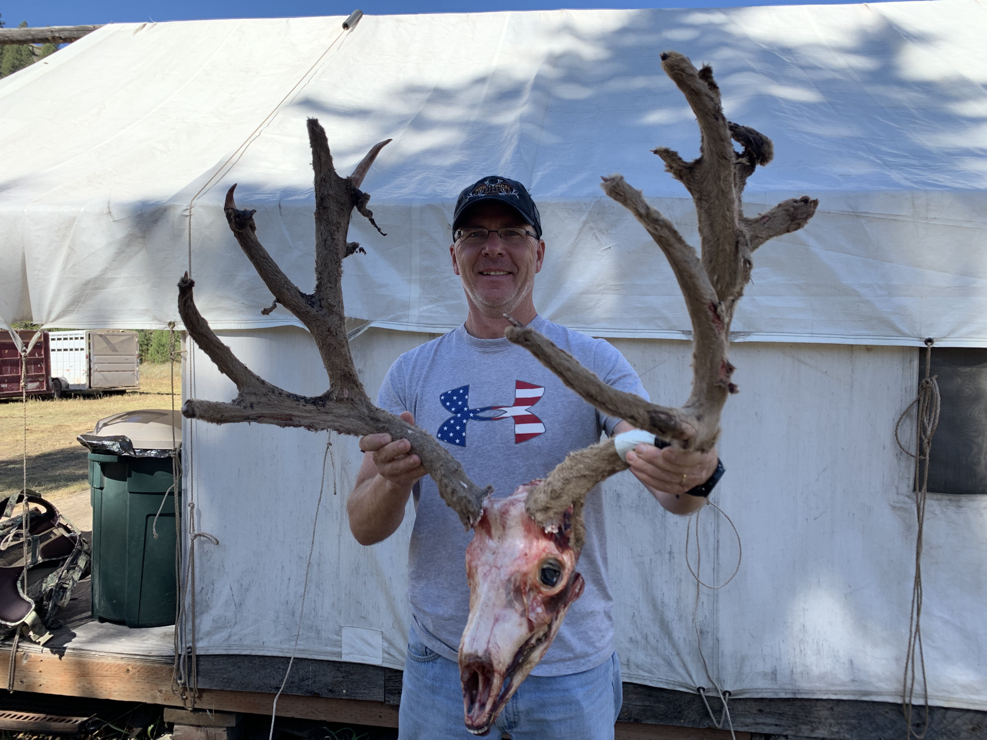 Man holding large deer antlers and skull in front of a white tent.