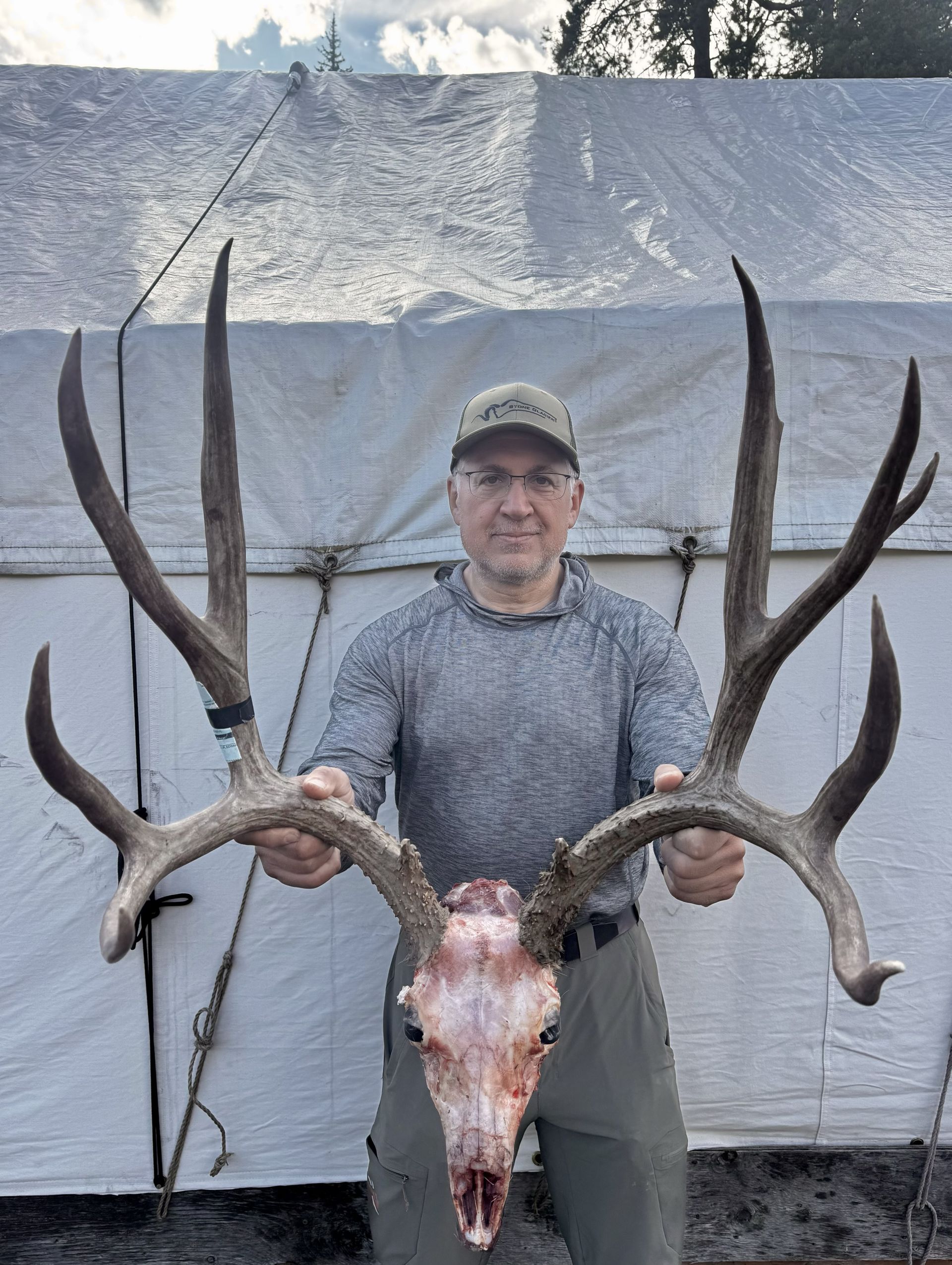 Man holding large deer antlers, with skull, in front of a white tent.