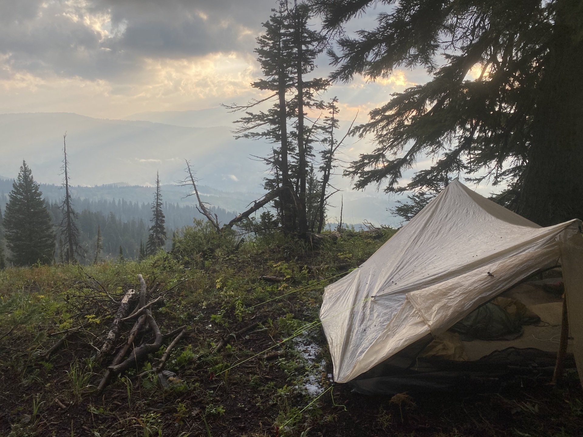 A tarp shelter set up in a forest, overlooking a misty mountain landscape at dusk.