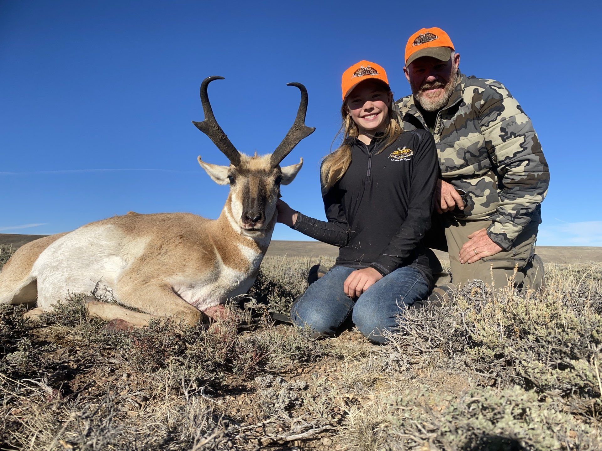 Hunter and young person kneel beside a trophy pronghorn antelope in a field.