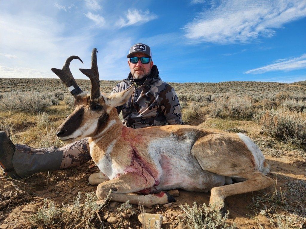 Hunter with a trophy pronghorn antelope in a sagebrush field under a blue sky. Antelope has large horns.