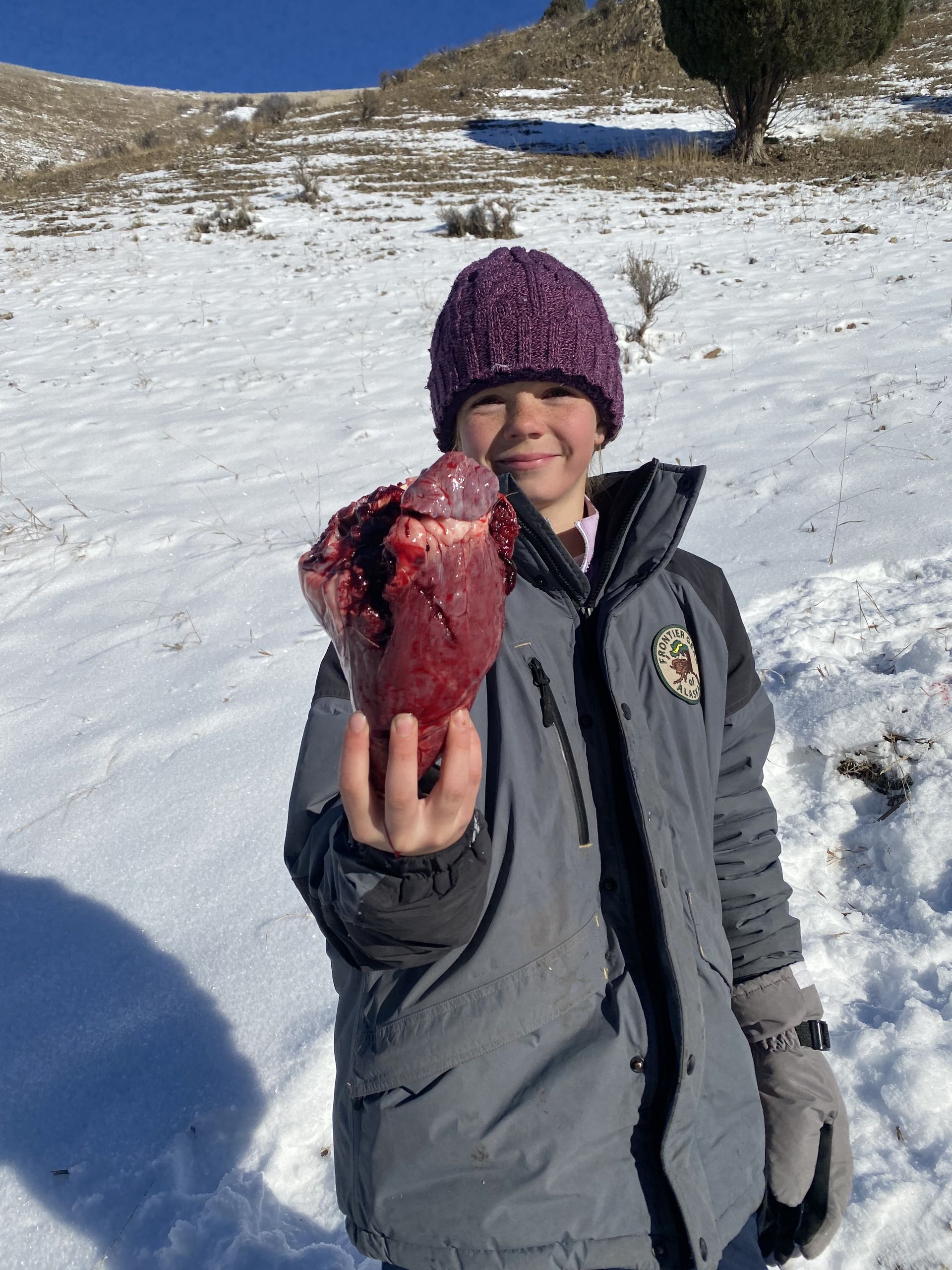 A young boy holding a piece of meat in the snow