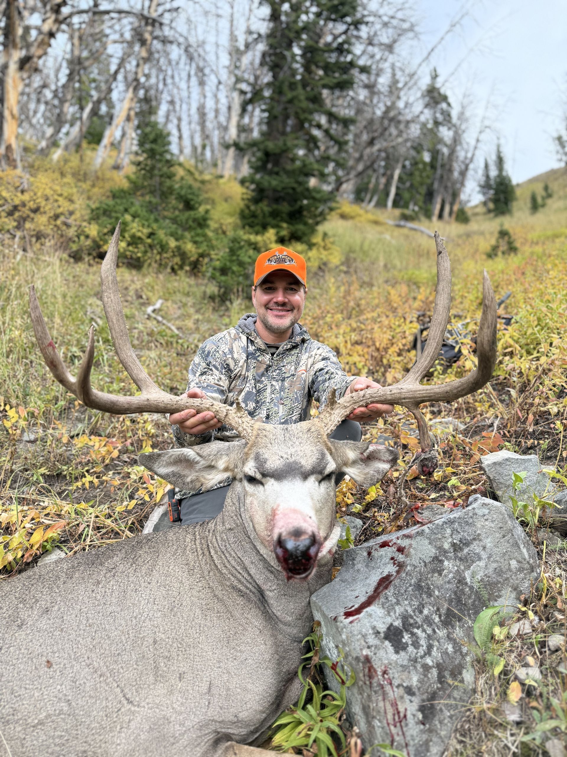 Man in orange hat and camo jacket holds antlers of a large buck.