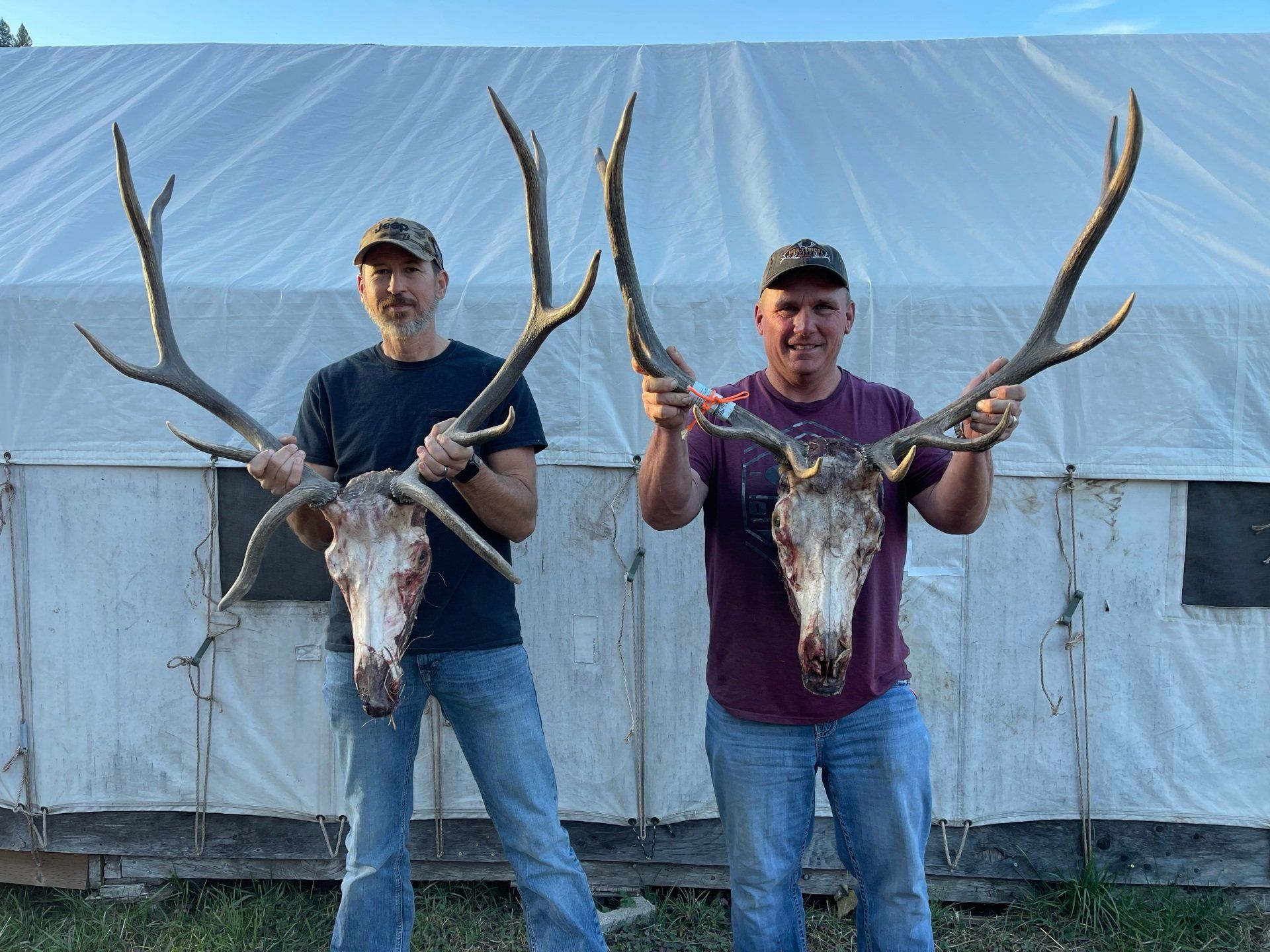 Two men standing next to each other holding deer antlers