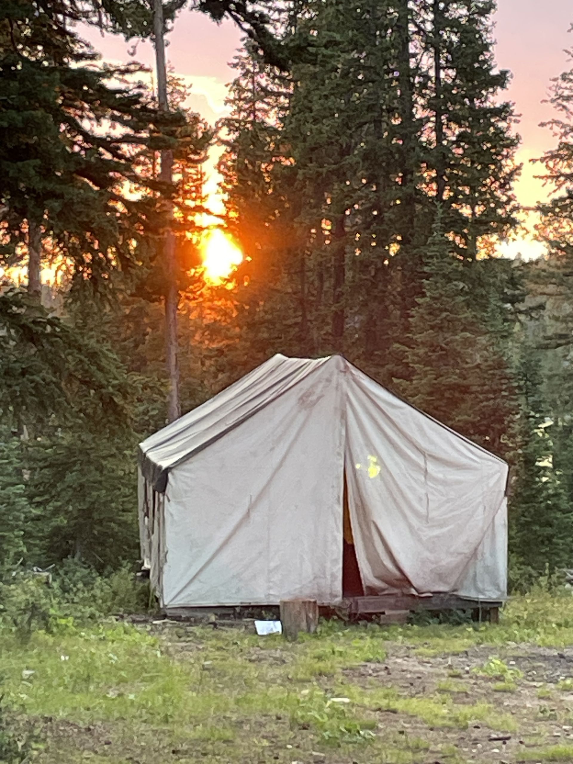 Canvas tent at dusk, surrounded by trees; sun setting with orange and yellow hues.