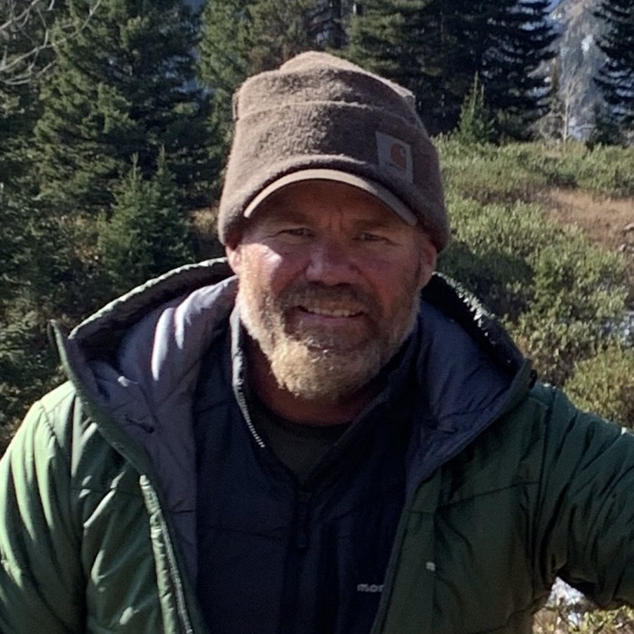 A man with a beard wearing a hat and a green jacket