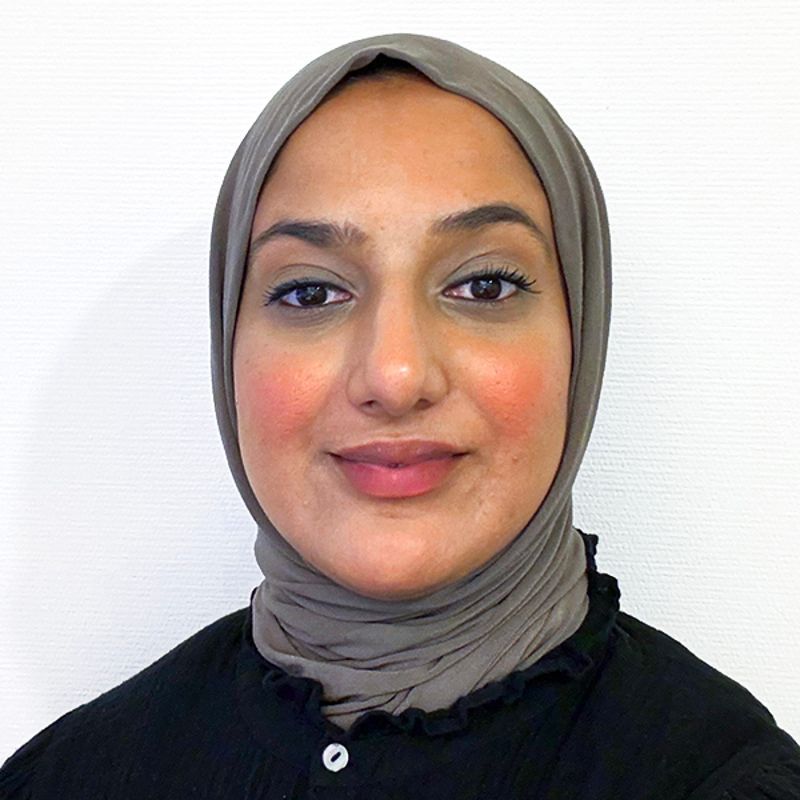 Woman with brown hijab and blush, smiling at the camera.