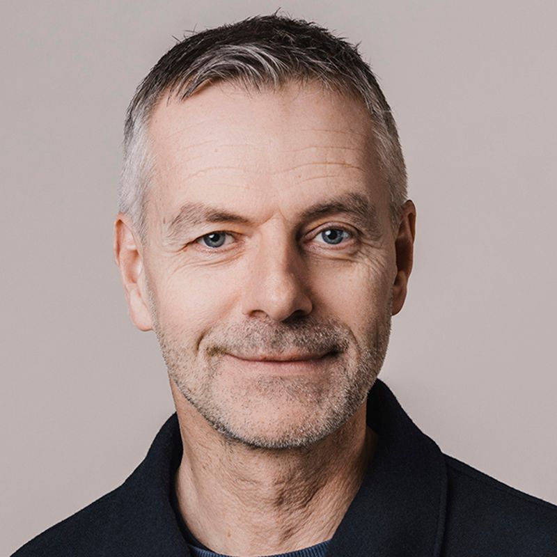 Man with graying hair, smiling, looking at the camera, wearing a dark jacket.