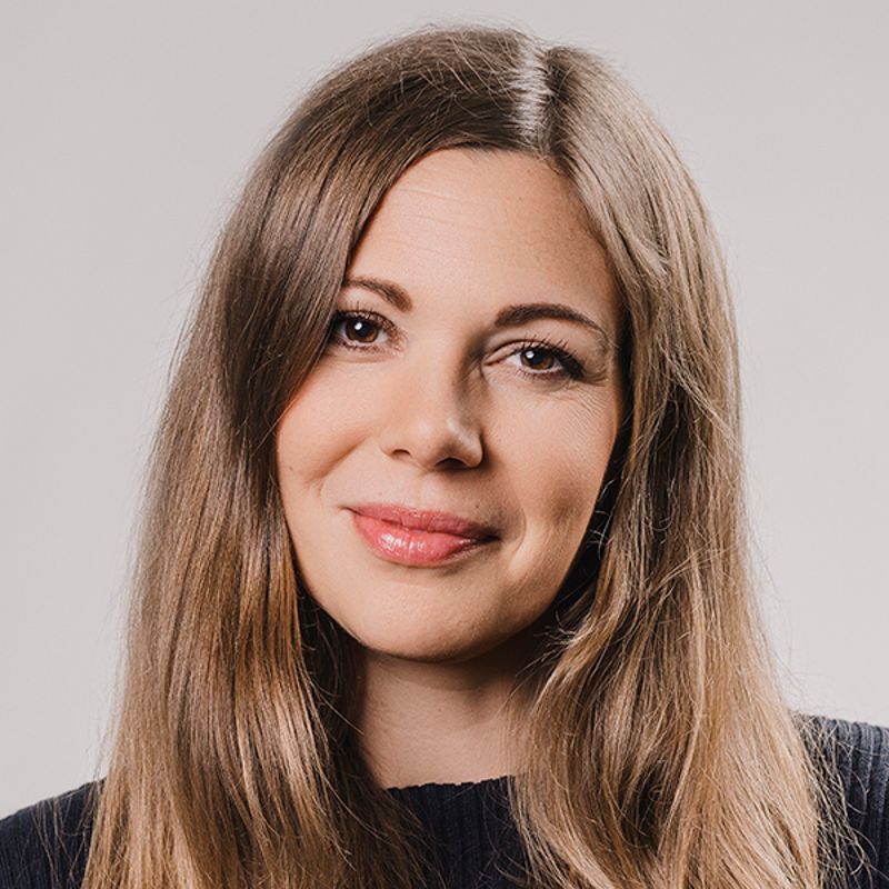 Woman with long brown hair, smiling, looking towards the camera.