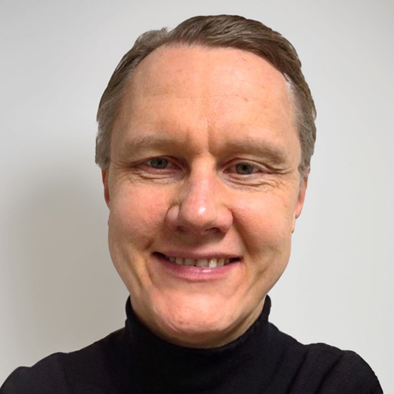 Man with light skin, smiling, wearing a black turtleneck.
