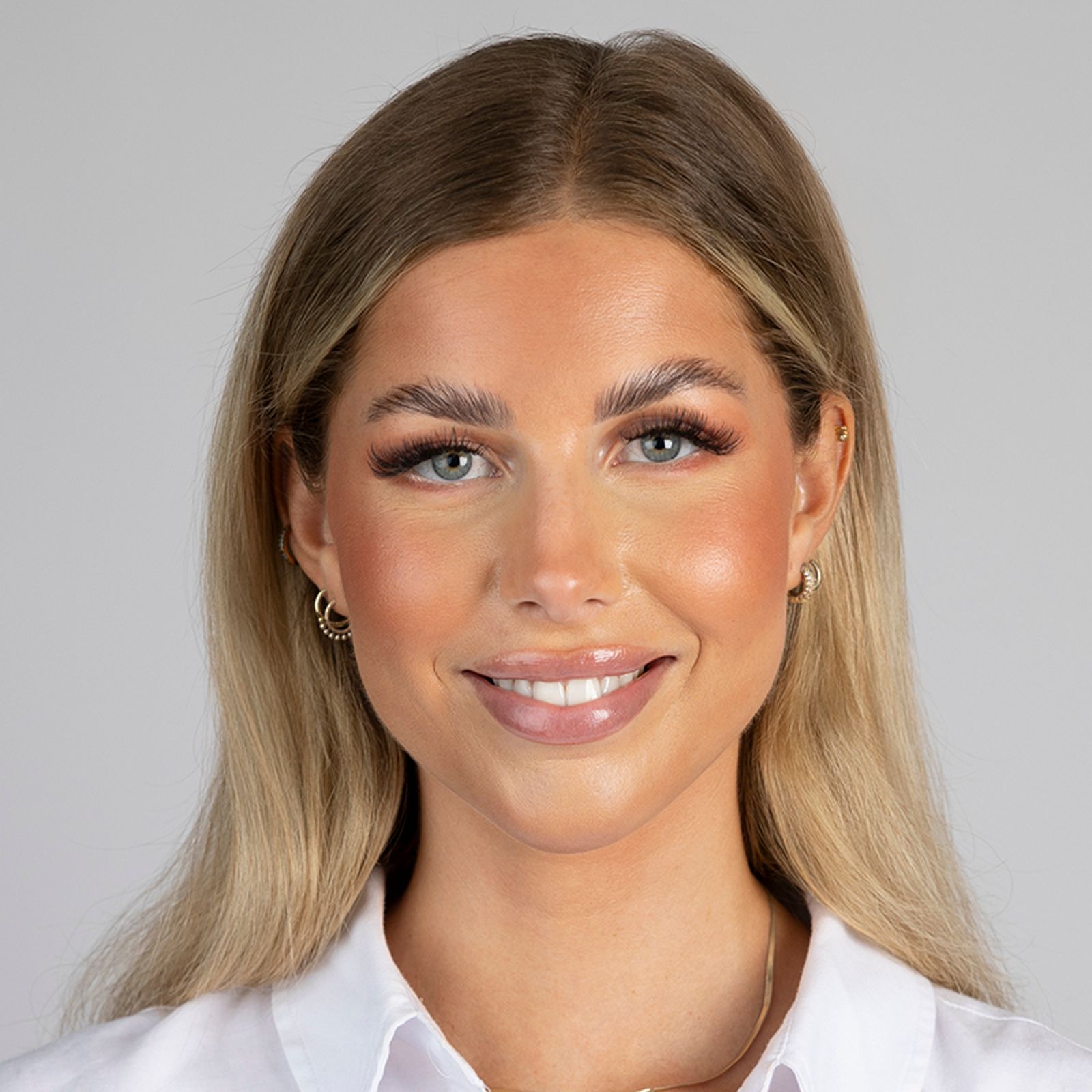 Woman with blonde hair, smiling, wearing a white shirt, on a gray background.