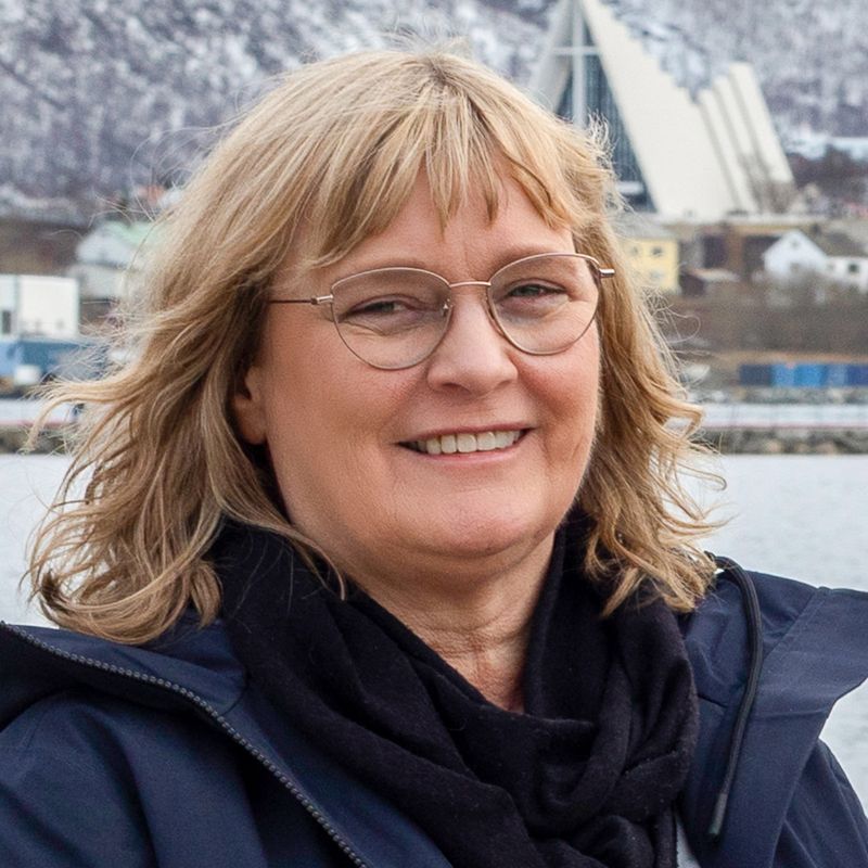 Woman with blonde hair and glasses smiles; Tromsø, Norway, in the background.