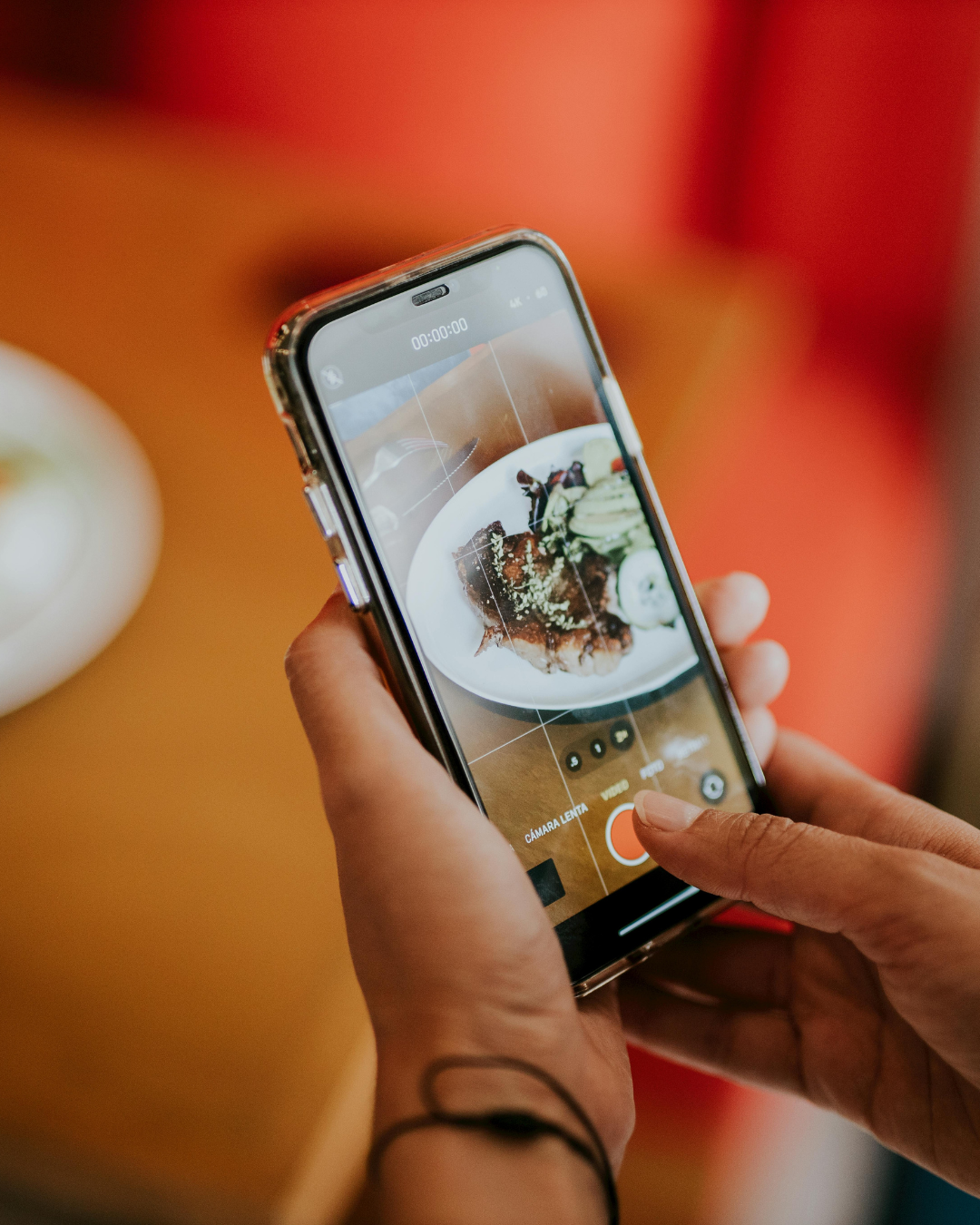 Hands holding a smartphone photographing a plated dish in a warm restaurant setting
