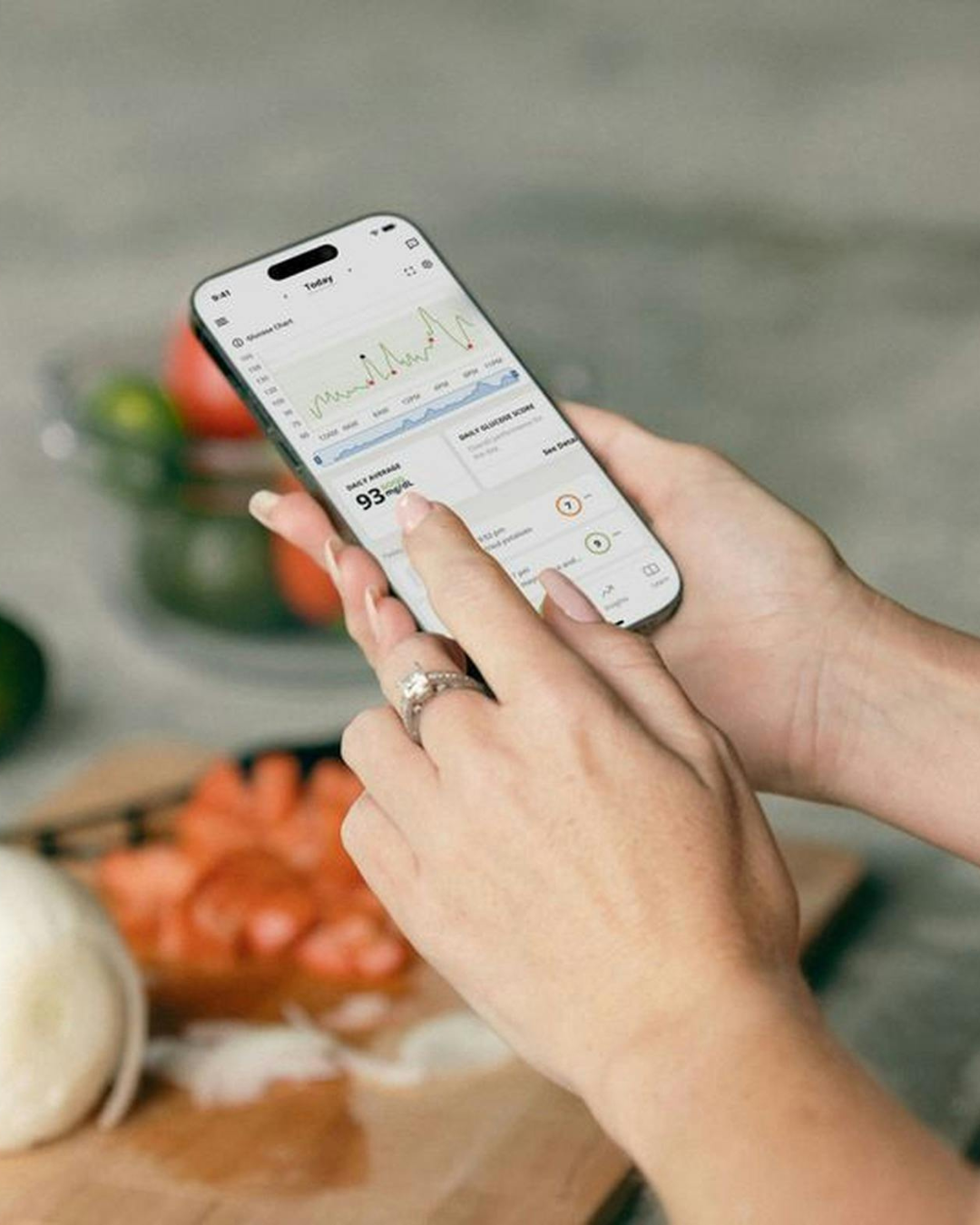 Hands using a smartphone beside fresh vegetables on a kitchen counter.