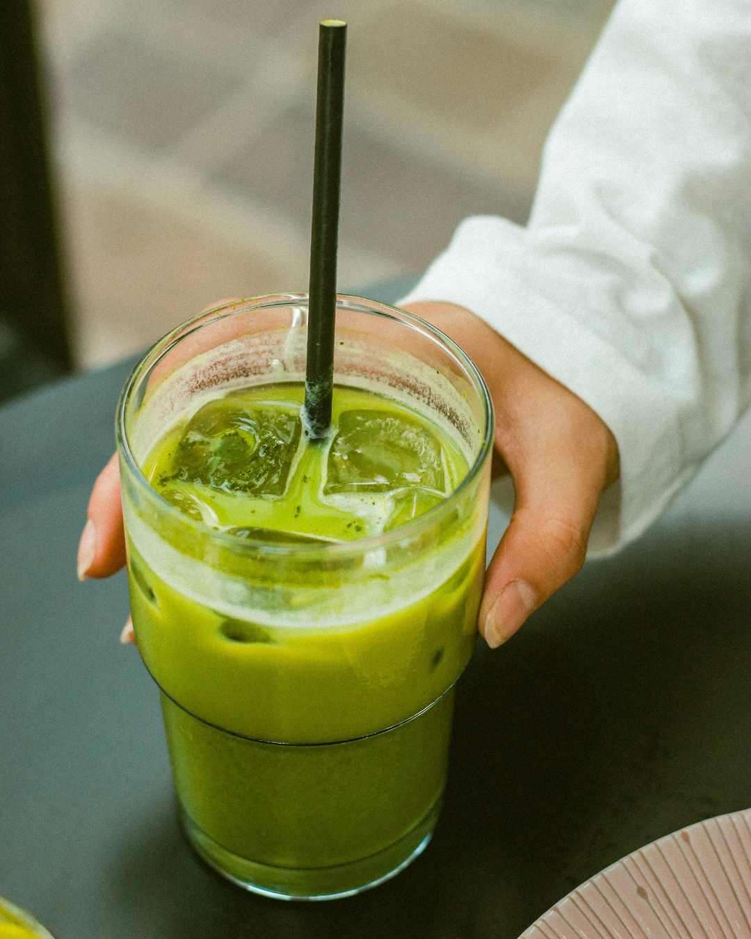 Hand holding a glass jar of green smoothie with a straw on a table