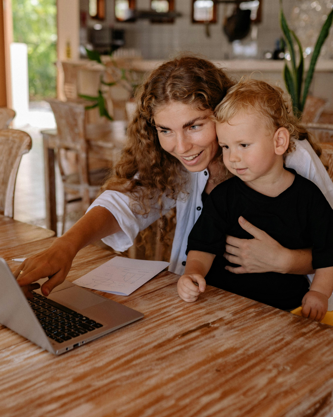 Woman and child at a wooden table looking at a laptop in a bright home interior