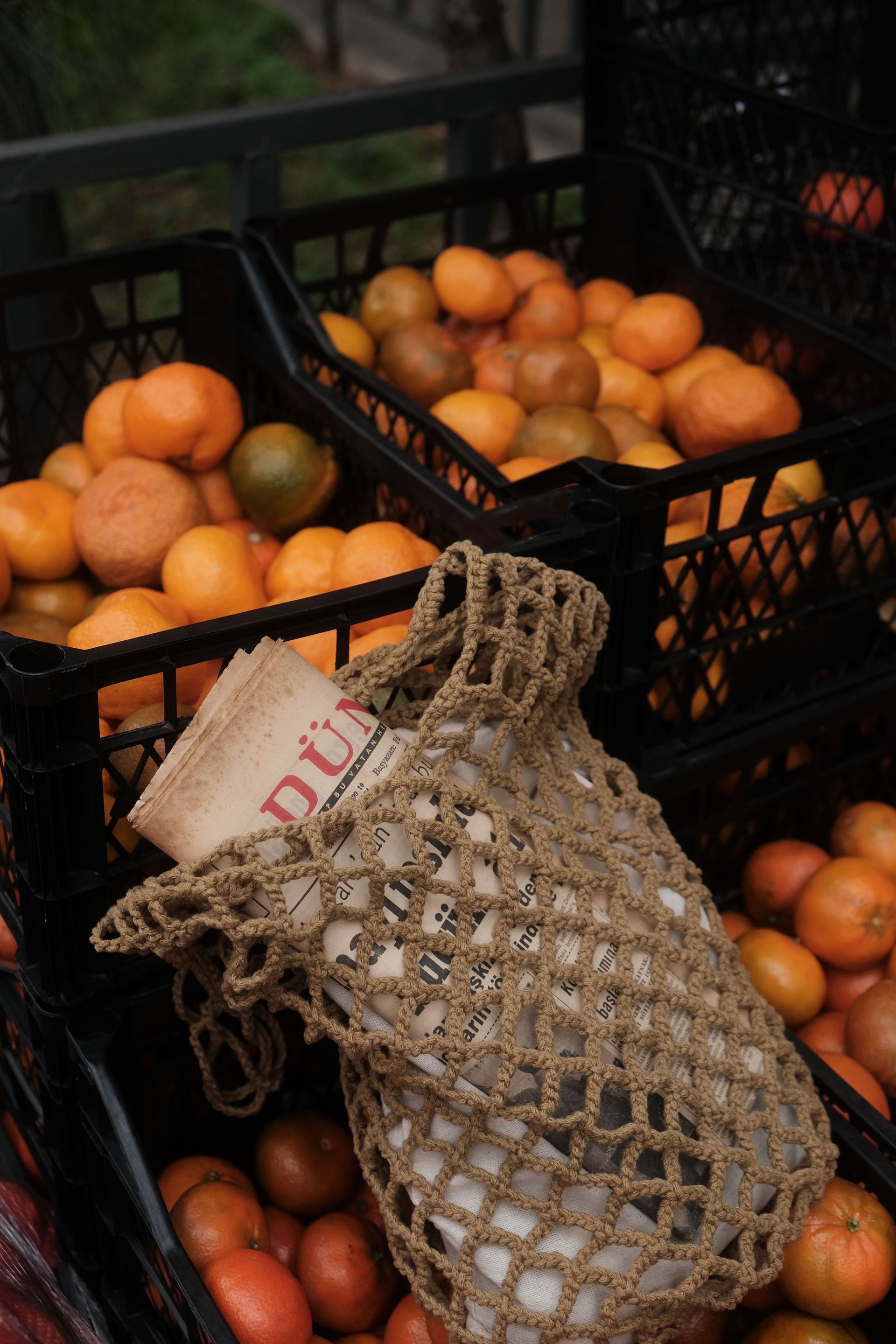 Crate of oranges with a mesh produce bag in front, stacked outdoors on a dark surface