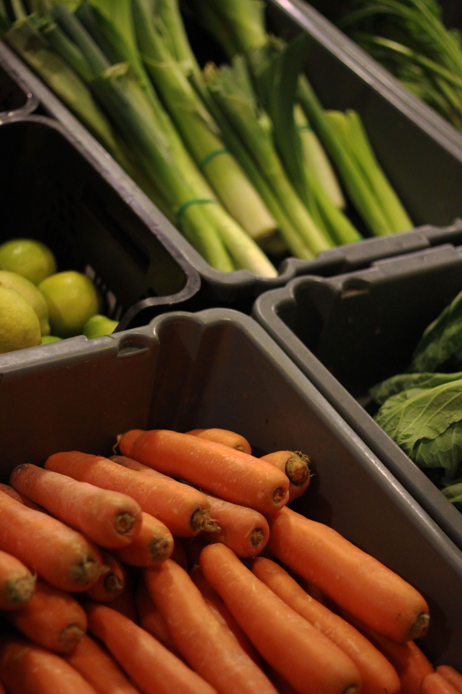 Fresh vegetables in produce bins, including carrots and green onions, at a market display