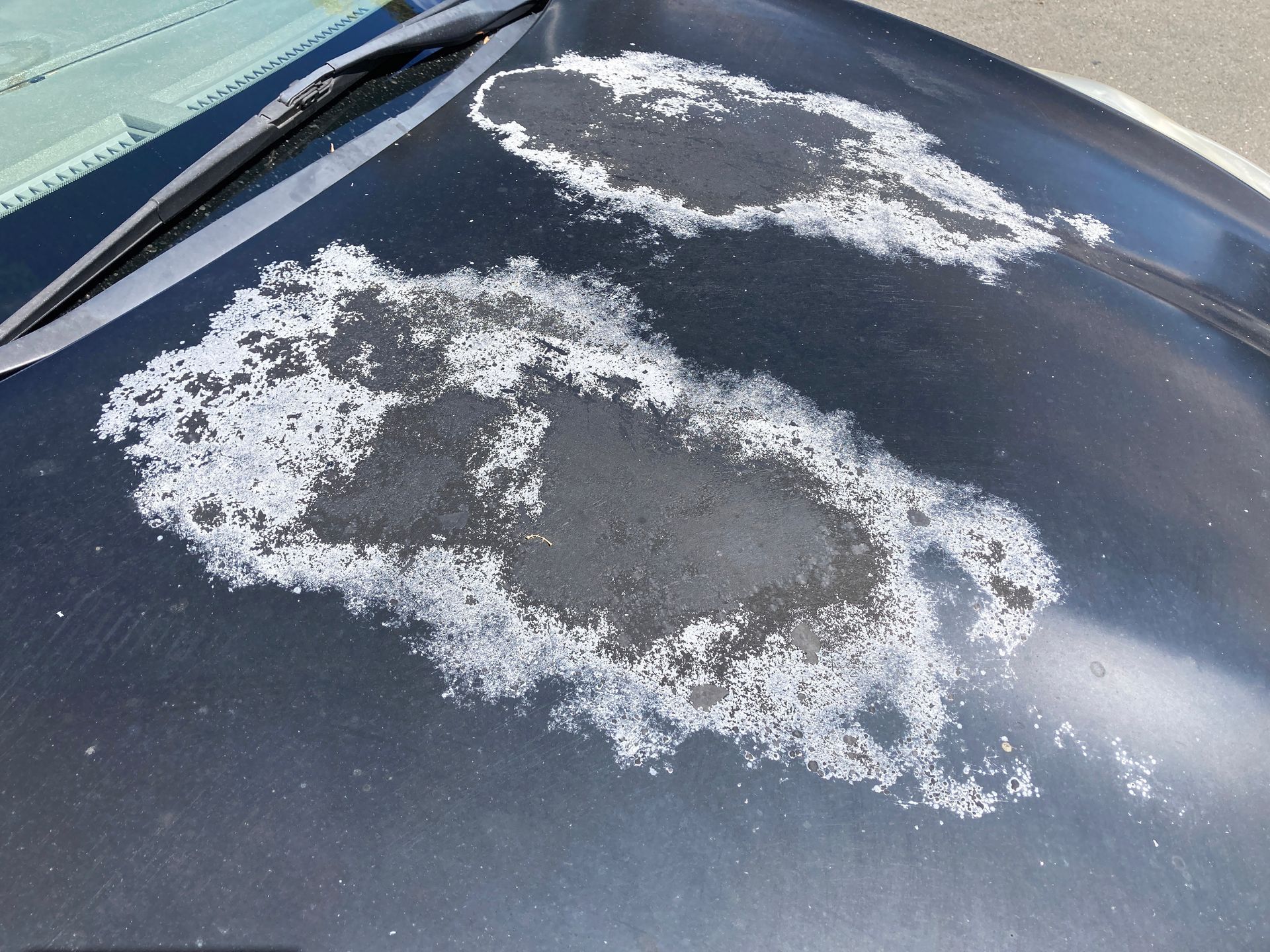 Peeling paint on a dark car hood, exposing white patches and bare metal underneath