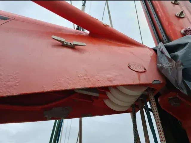 Primer plano de una estructura metálica roja de un puente con pernos y cables contra un cielo nublado.