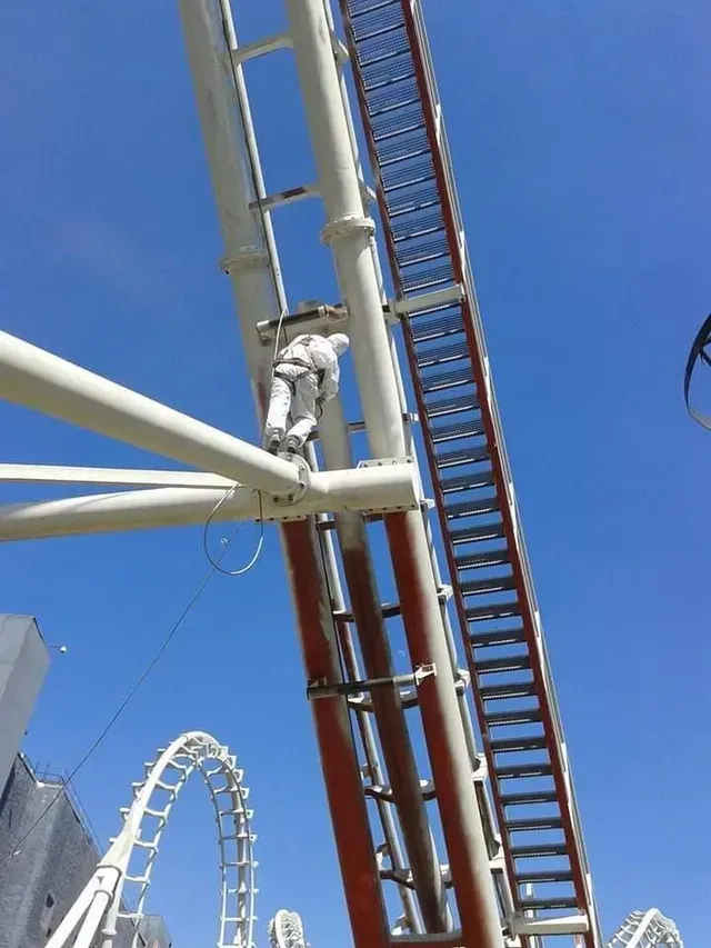 Un trabajador trepa a la estructura de una atracción de un parque de diversiones.