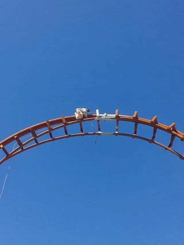 Una vía de montaña rusa se curva contra un cielo azul despejado, con un pequeño vagón en la cima.