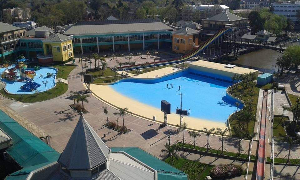 Parque acuático al aire libre con grandes piscinas azules, palmeras y edificios circundantes.