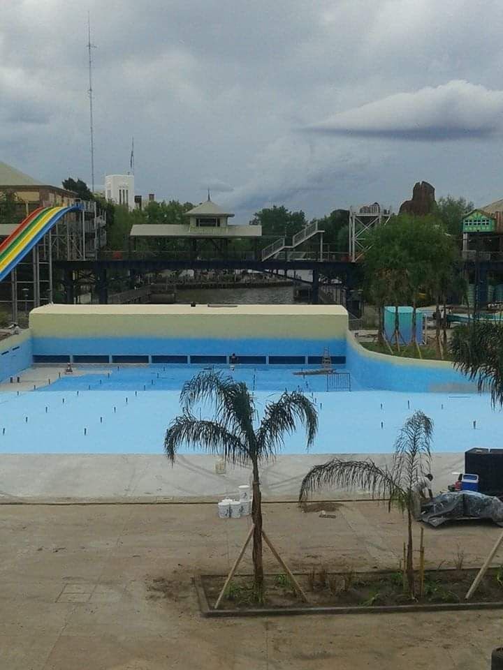 Parque acuático al aire libre con una gran piscina azul vacía, toboganes y cielo nublado.