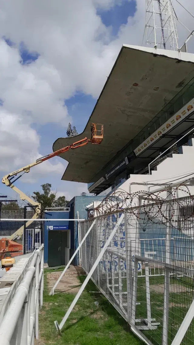 Un elevador de construcción trabajando junto al techo de un gran estadio bajo un cielo nublado.