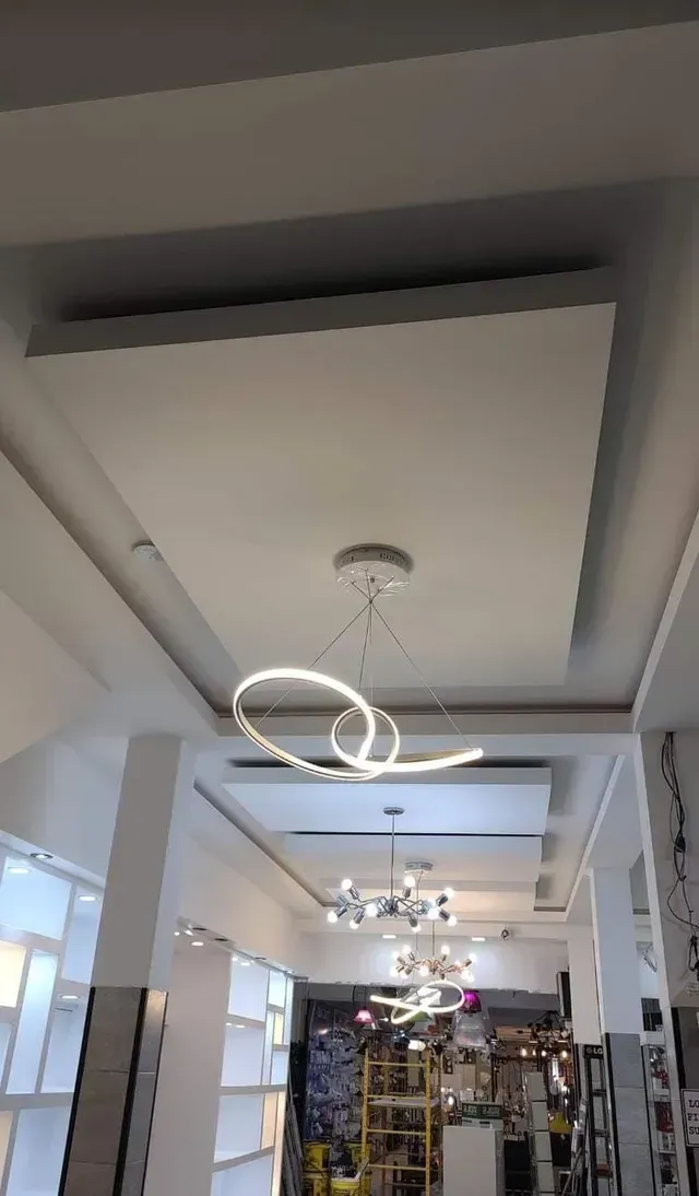 Interior luminoso y moderno con techo empotrado, lámpara de araña circular y percheros en un espacio comercial.