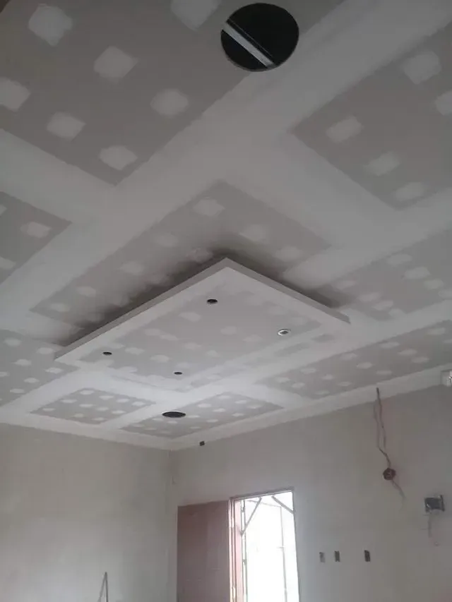 Habitación sin terminar con techo de pladur, luces empotradas y una ventana pequeña.