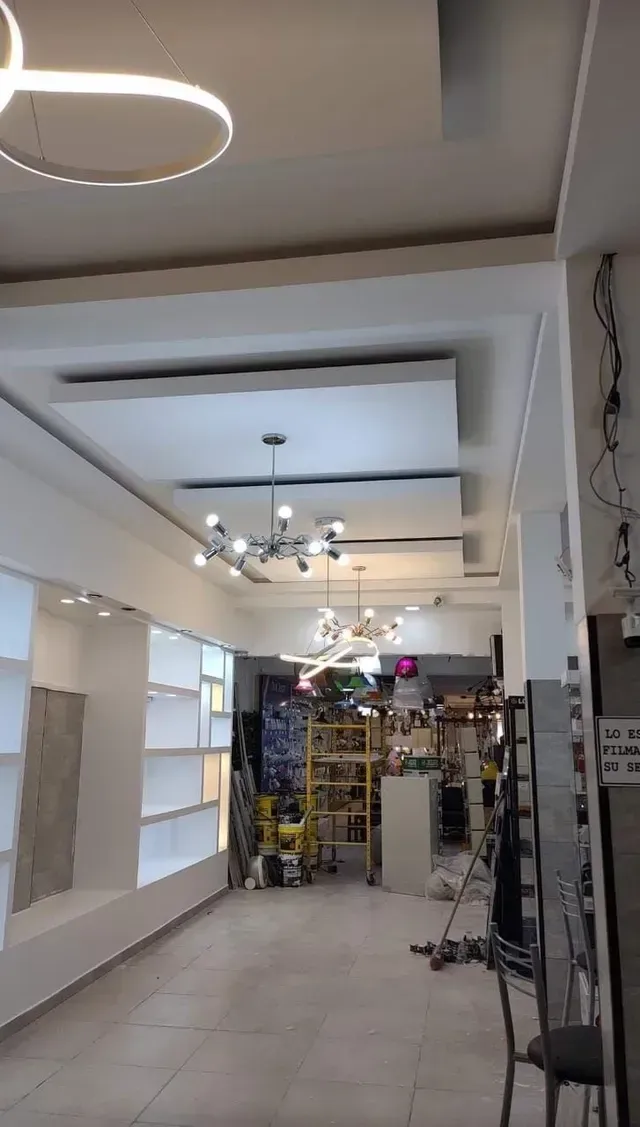 Sala de exposición luminosa y vacía, con paredes blancas, lámparas de araña y estanterías a lo largo de un pasillo alicatado.