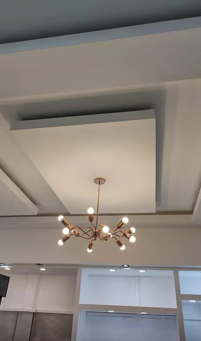 Techo moderno con paneles empotrados y una lámpara de araña central en una habitación luminosa.